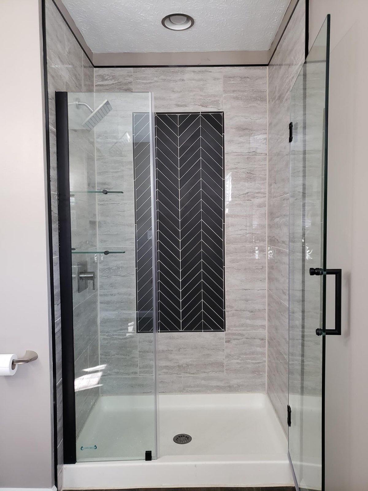 Travertine look shower walls with a black herringbone accent panel, finished with custom glass through our glass partner