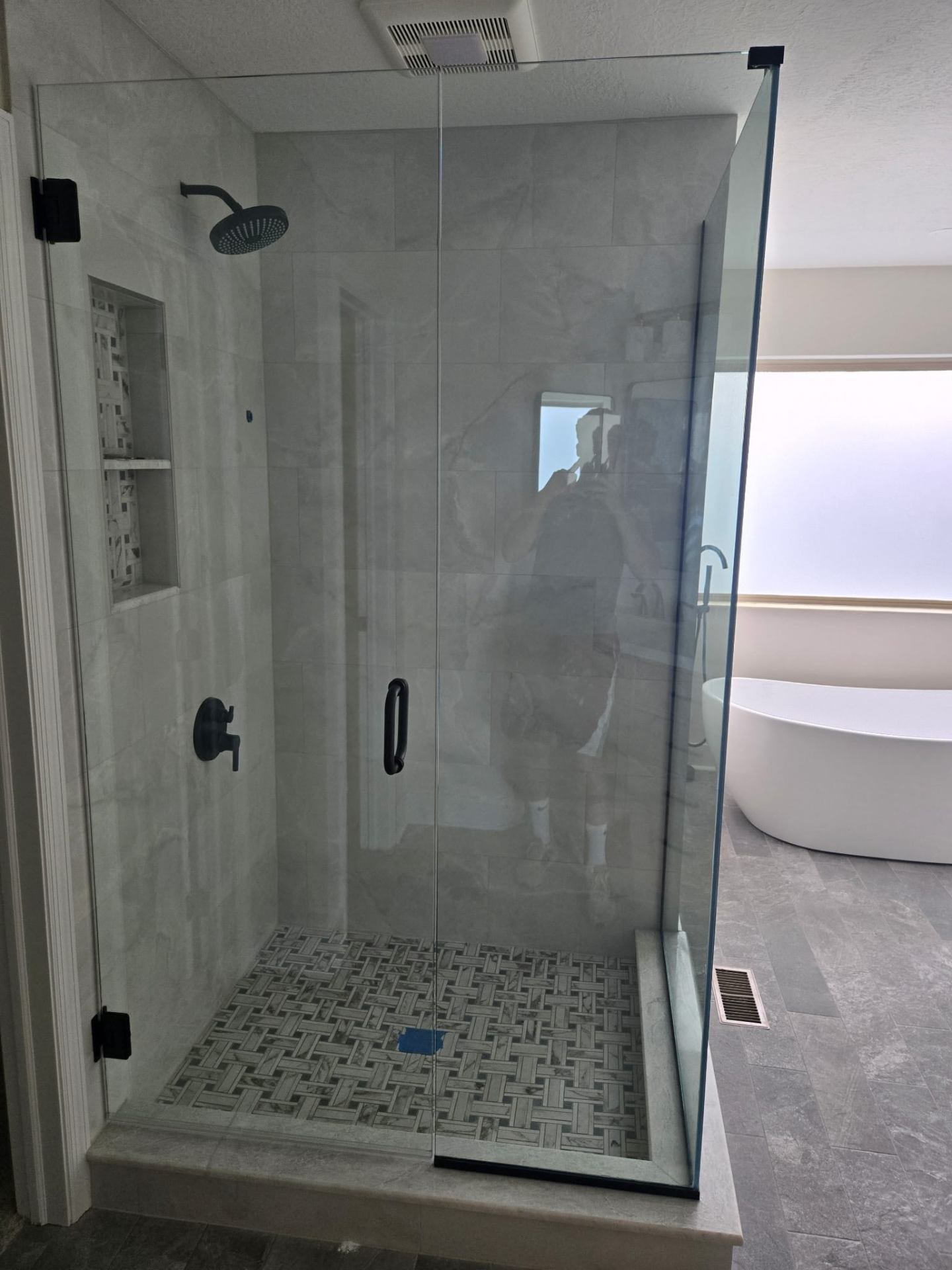 Walk in shower with marble look porcelain walls, basketweave mosaic floor, and tiled niche, finished with custom glass through our glass partner