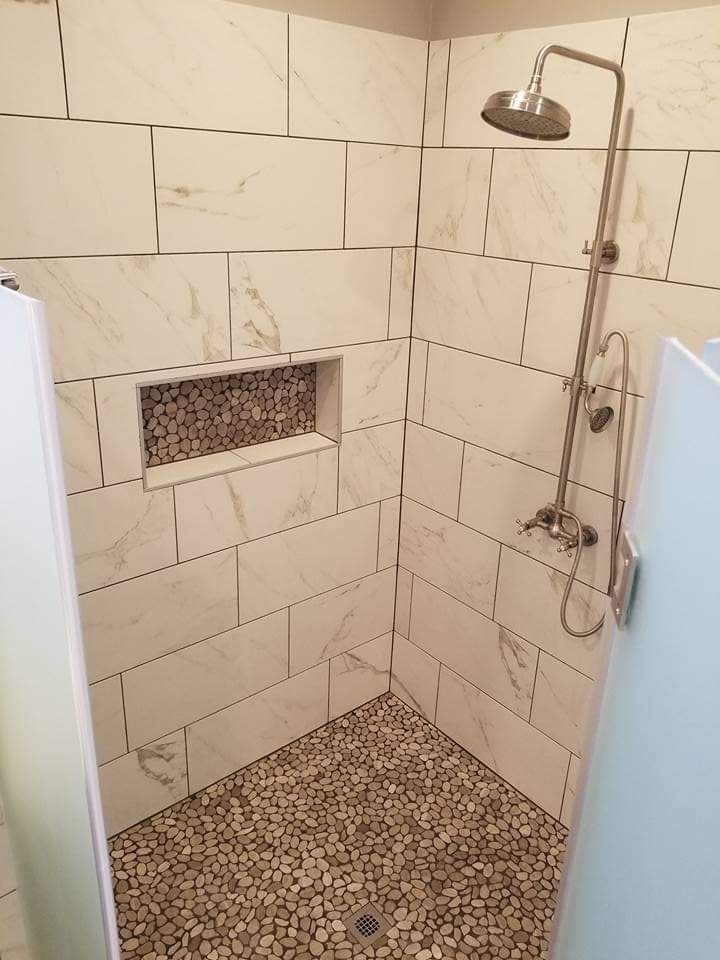 Marble look porcelain shower walls with a pebble mosaic floor and matching pebble niche