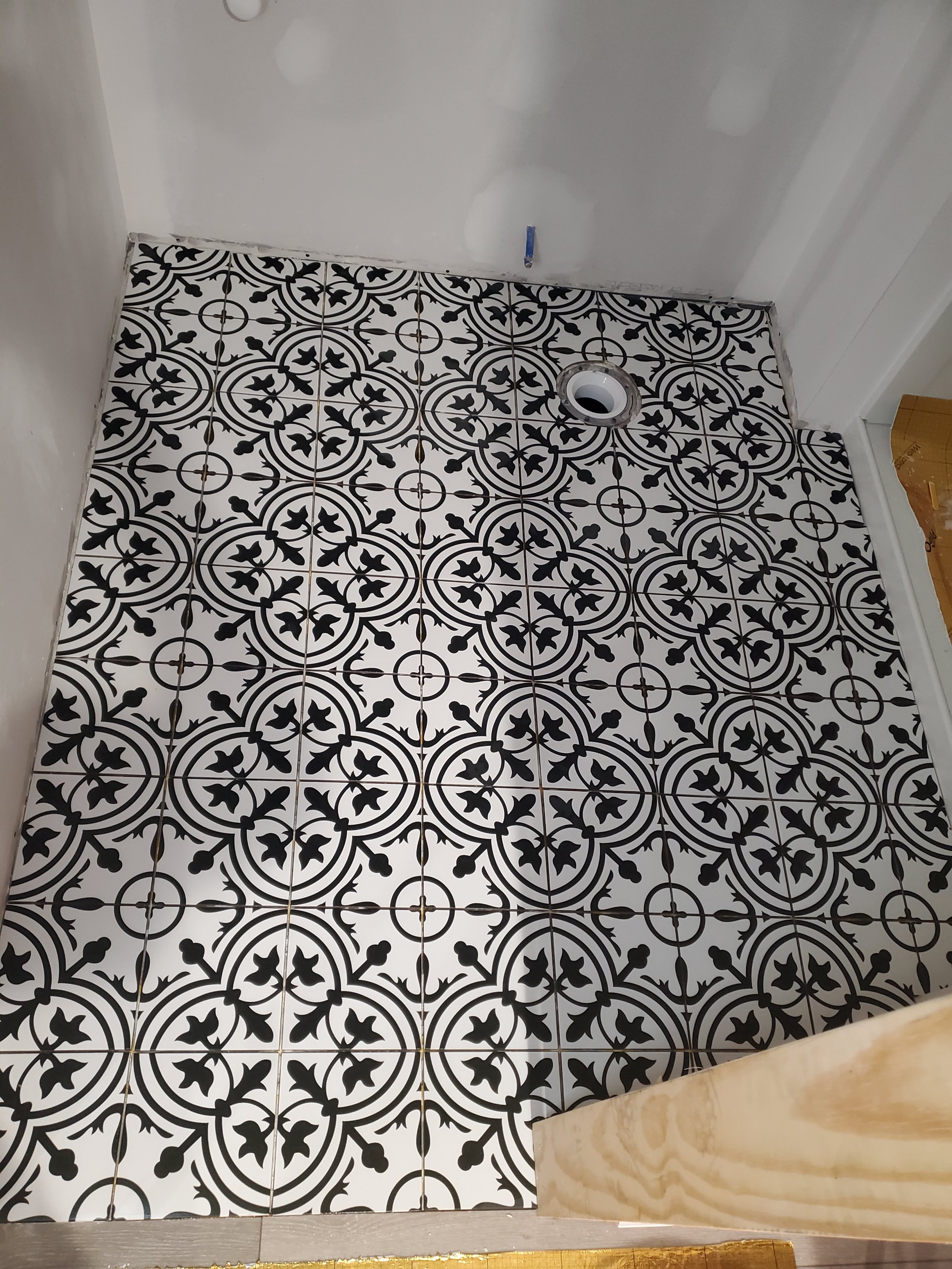 Black and white patterned porcelain bathroom floor tile, set before fixtures