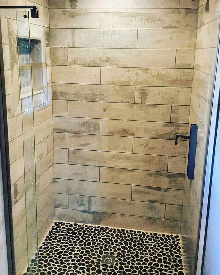 Wood look plank tile shower walls with a black pebble mosaic floor