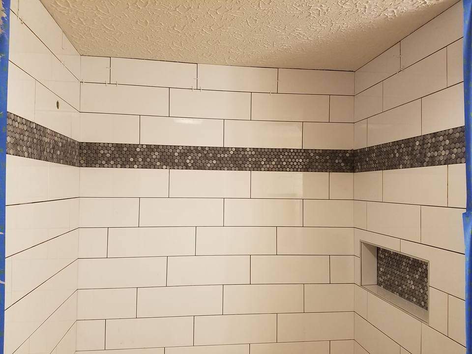 Subway tile shower walls with a penny tile accent band and matching niche, during installation