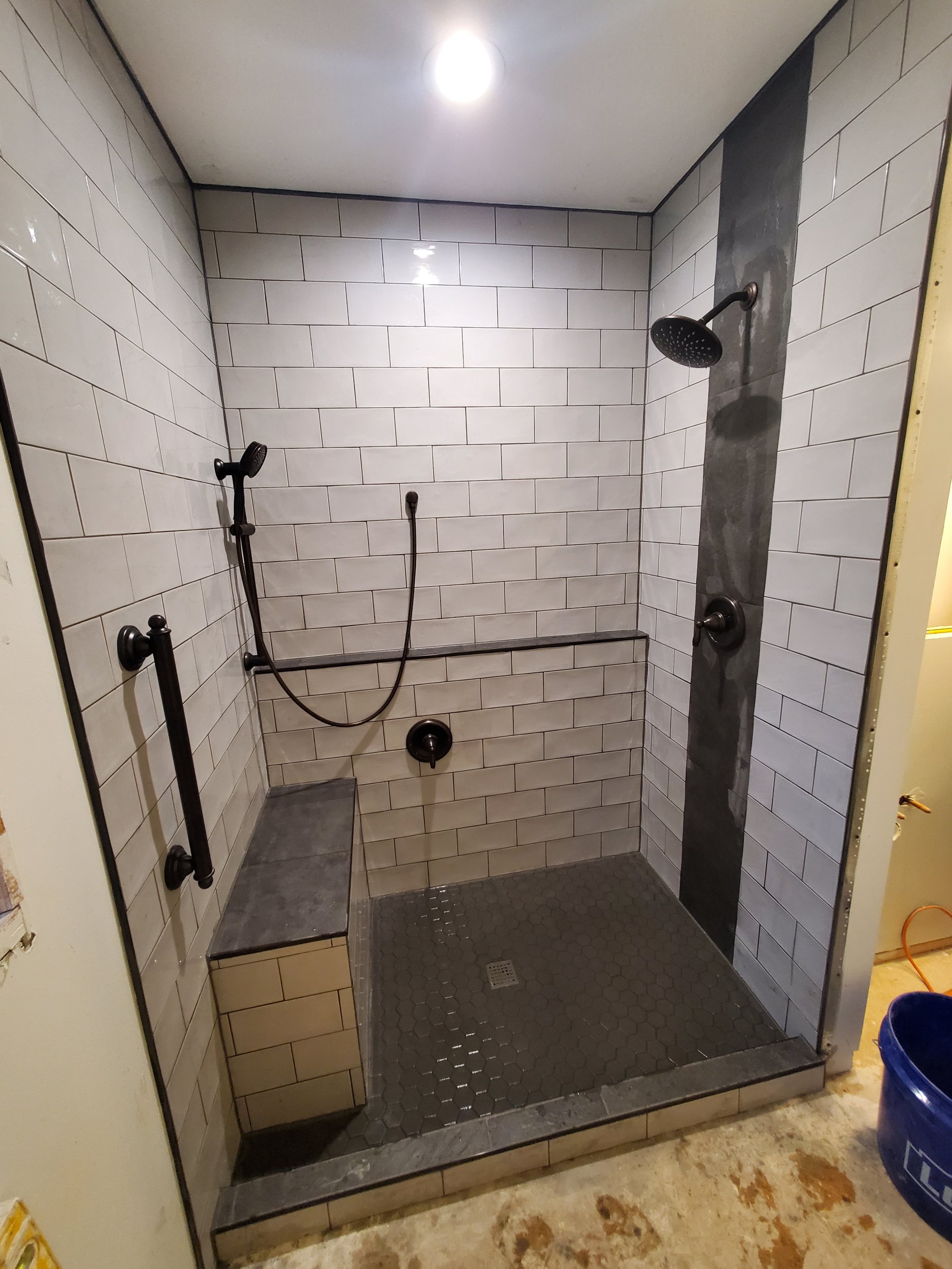Tile shower with built in bench, grab bar mounted through tile, and slate look accent column