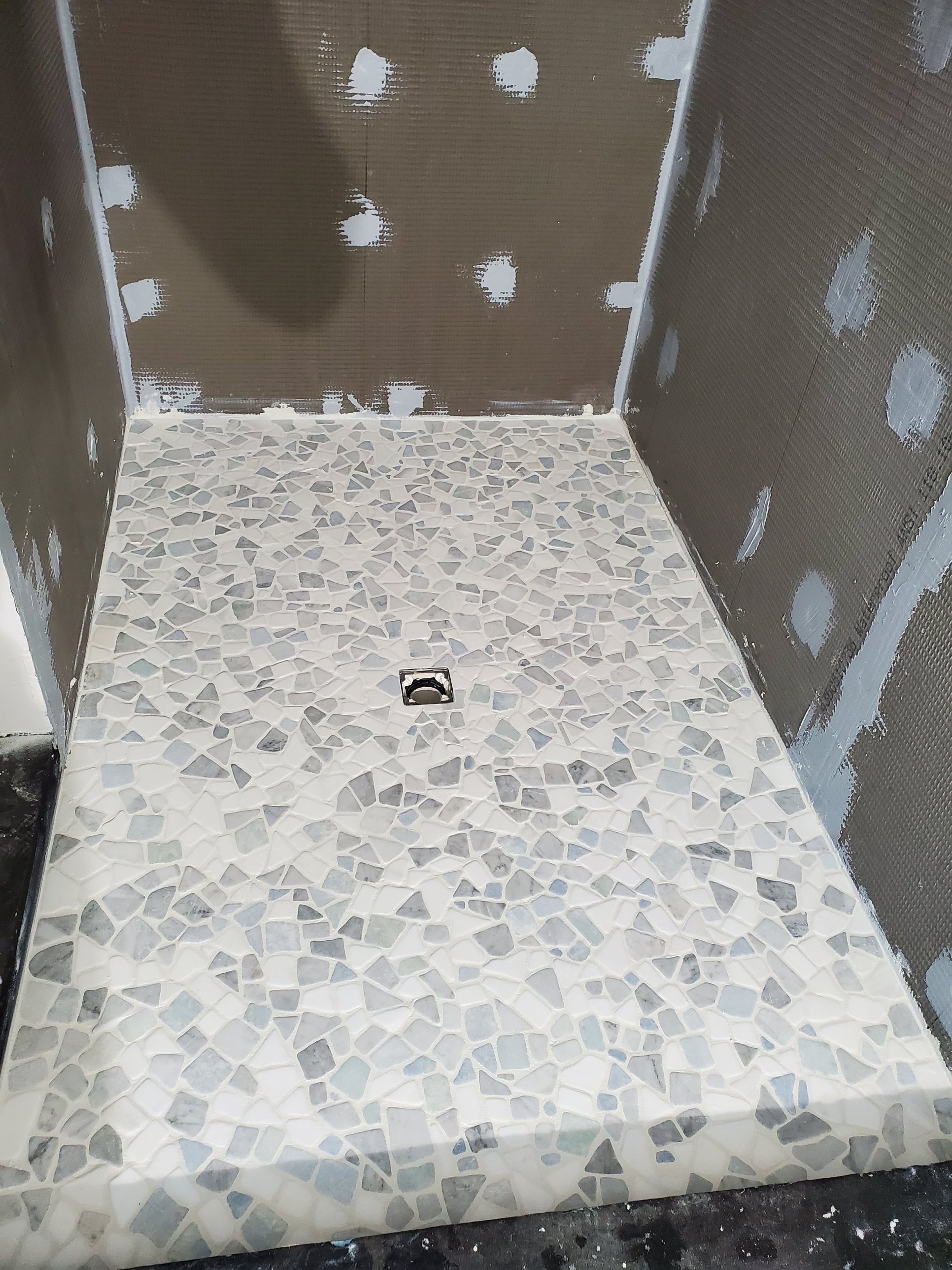 Marble pebble mosaic shower floor set over Wedi waterproofing board before the walls are tiled